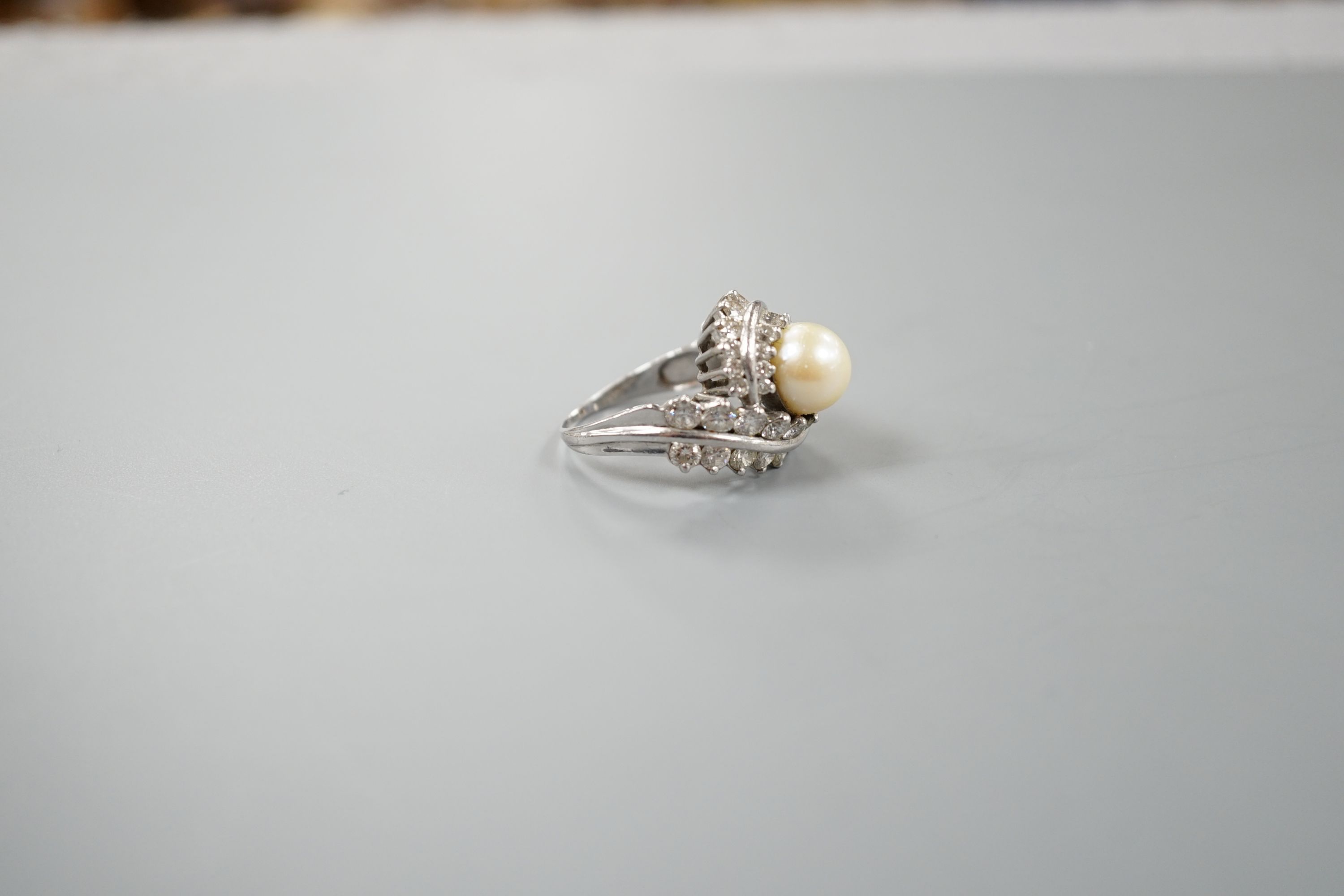 A white metal single stone cultured pearl and diamond cluster set scroll dress ring, size Q, gross weight 13.6 grams.